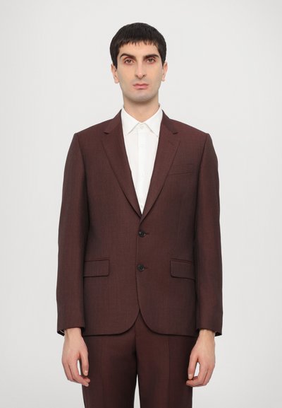 Costume sur mesure bordeaux avec un devant à deux boutons, des revers crantés et une coupe structurée. Accompagné d'une chemise blanche à col en dessous.