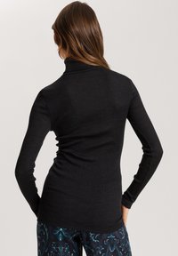 Schwarzer Rippstrick-Turtleneck-Pullover mit langen Ärmeln und taillierter Silhouette, kombiniert mit gemusterten Hosen.