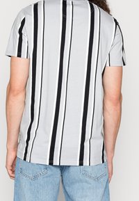 Grå kortärmad t-shirt med vertikala svarta och vita ränder, rund halsringning och avslappnad passform. Bakifrån syns nederkanten vid höftnivå.