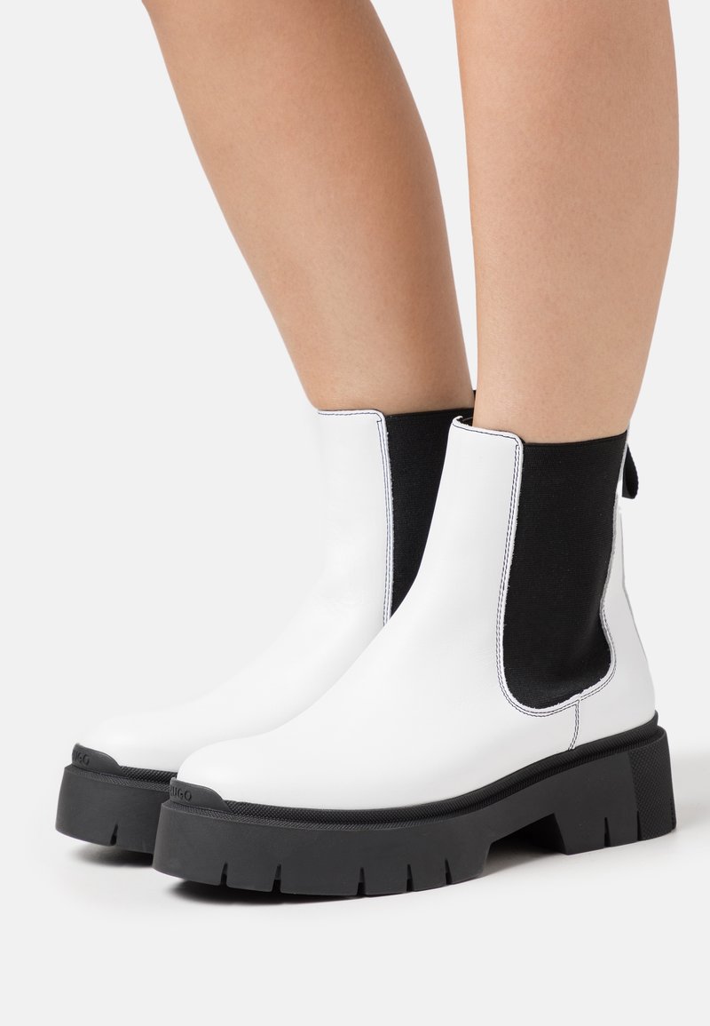 Bottes Chelsea en cuir blanc avec panneaux latéraux élastiques noirs, semelles épaisses en caoutchouc noir et coutures blanches contrastantes le long des bords.