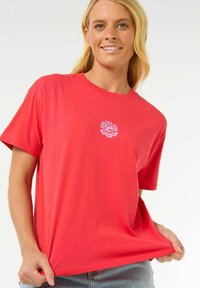 T-shirt rouge en coton doux, avec un petit design de logo blanc au centre. Manches courtes et coupe décontractée.