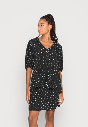 Vestido preto com bolinhas brancas, apresentando um decote em V, mangas curtas bufantes e um design em camadas, com uma textura flutuante e um brilho sutil.