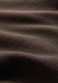 Tmavohnedá tkanina s mäkkým, textúrovaným povrchom, s jemnými vlnkami a drobnými vláknami. Žiadne výrazné vzory ani akcenty nie sú viditeľné.