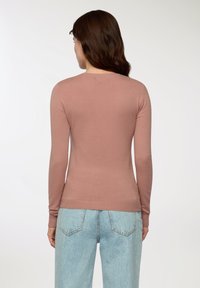 Różowy wełniany sweter z długim rękawem i okrągłym dekoltem, z prążkowanymi mankietami i dołem. Noszony z jasnoniebieskimi dżinsami o wysokim stanie.