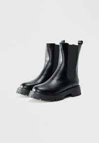 Botoșei negri din piele cu glezna, cu panouri elastice pe laterale, vârf rotunjit și talpă groasă, din cauciuc cu textură. Design minimalist cu detaliu de mânere.