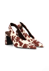 Zapatos de tacón alto tipo slingback con punta afilada, en una base blanca con un patrón de piel de vaca marrón. Tela texturizada y diseño de tacón grueso.