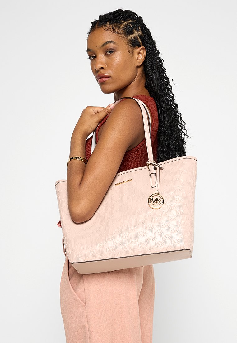 Bolso tote de color rosa claro con un acabado texturizado, herrajes dorados y un charm con el logo. Presenta asas resistentes y una forma estructurada.