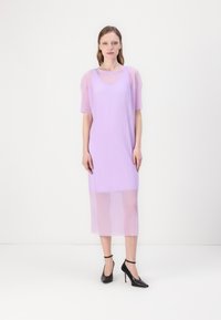 Laventelivihreä ribbed midi-mekko lyhyillä hihoilla ja läpikuultavalla päällisellä. Mustat korkokengät korostavat asua. Yksinkertainen, suora leikkaus.