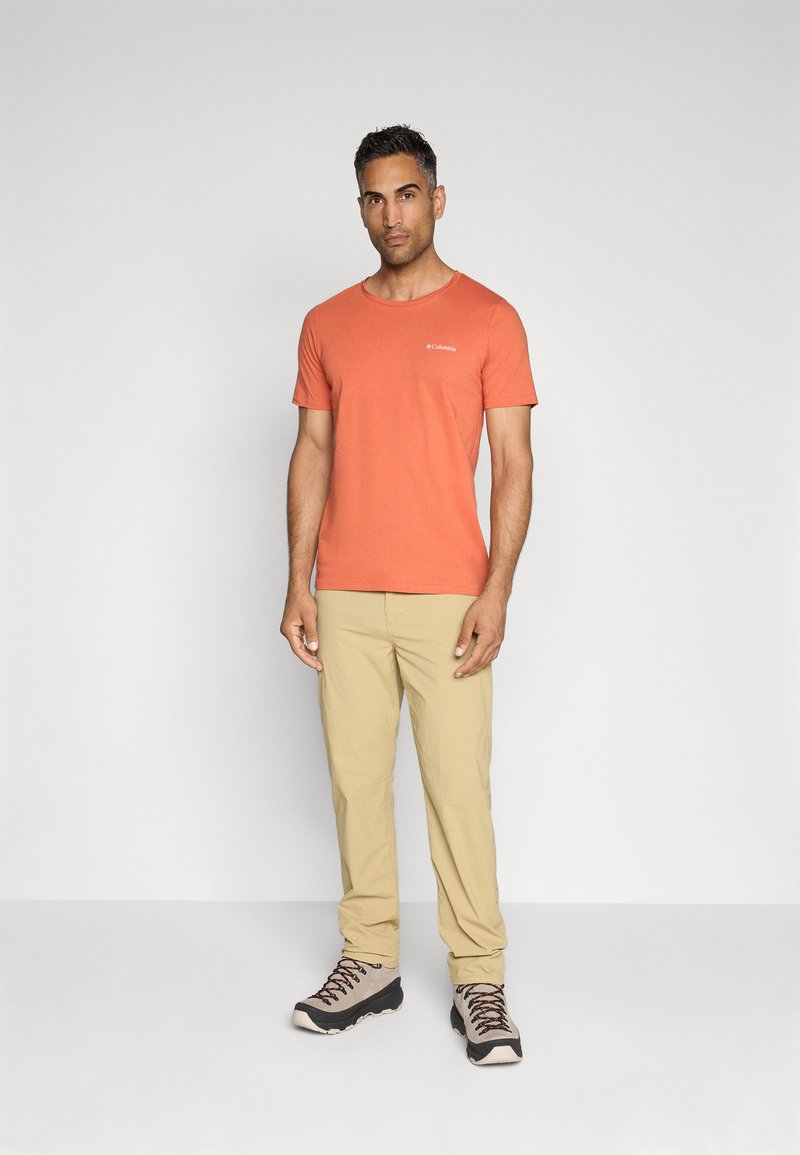 Oranges Crew-Neck T-Shirt mit kurzen Ärmeln, kombiniert mit beigen Hosen und grauen Wanderschuhen mit schwarzen Akzenten und Schnürsenkeln.