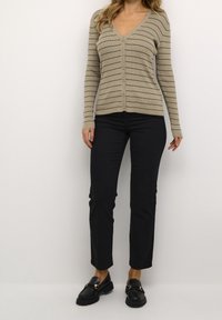 Beige ribbed cardigan with dark horizontal stripes, V-neckline, front buttons; paired with black slim-fit pants and black loafers.