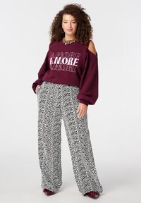 Bordeauxrode trui met uitgesneden schouders en een gedurfde "AMORE"-tekst. Zwart-witte zebra gestreepte broek met wijde pijpen en een zachte textuur.