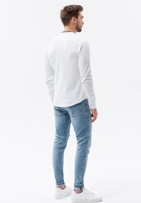 Camisa blanca de manga larga y vaqueros claros desgastados. Zapatillas blancas. La camisa presenta un diseño liso con un detalle de cuello en contraste.