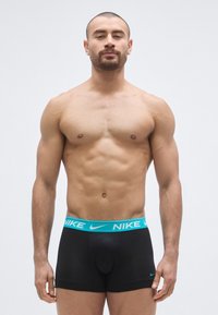 Μαύρα ανδρικά μπόξερ με φαρδύ λογότυπο της Nike σε τιρκουάζ στη μέση, με εφαρμοστή σχεδίαση και μεσαίο μήκος ποδιού. Μαλακή υφή ύφασματος.