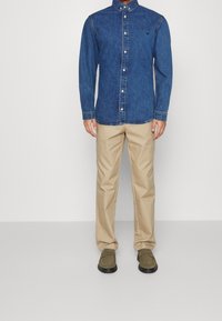 Jeansskjorta i mörkblått med knappstängning, i kombination med ljusbeige byxor och olivgröna skor med svart sula.