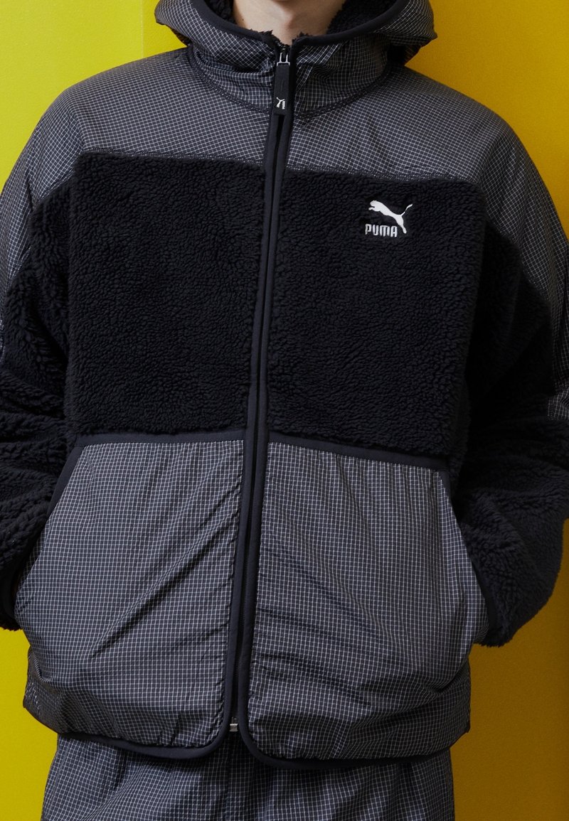 Sort og grå zip-up jakke med tekstureret fleece og trykt stof. Har en høj krave og brandlogo på brystet.