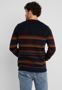 Navy Pullover mit mehrfarbigen geometrischen Mustern in Rot, Orange und Blau über der Brust und an den Ärmeln. Rippbündchen und Saum.