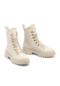Beżowe skórzane buty wojskowe z futrzanym wykończeniem, sznurowane, z metalowymi detalami i masywną gumową podeszwą. Posiadają uchwyt z tyłu.