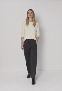 Beige stickad tröja med långa ärmar kombinerad med högmidjade svarta byxor med dragsko i midjan. Bär svarta ankelboots.