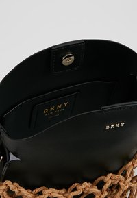 Czarna skórzana torba na ramię z plecionym brązowym uchwytem, magnetycznym zapięciem i złotym logo w środku. Wnętrze zawiera przegródki na karty.