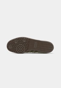 Sport shoe sole in dark brown rubber, featuring a textured pattern with circular and triangular designs, and green fabric side accents.