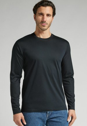 Schwarzes Langarmshirt aus glattem Stoff mit Rundhalsausschnitt, mit taillierter Form und schlichtem Design, kombiniert mit Jeans.