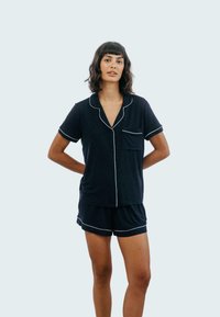 Conjunto de pijama de manga corta en azul marino con ribetes blancos. La parte superior cuenta con un cierre de botones en el frente y un bolsillo en el pecho. Los pantalones cortos son a juego.