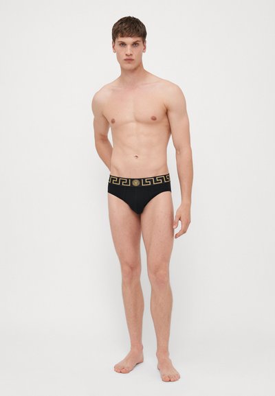 Zwarte zwembroek met een gouden geometrisch patroon op de tailleband. Gemaakt van een gladde stof, met een snug en contoursnit.