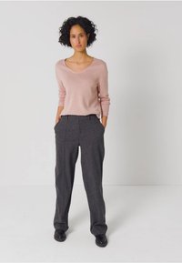 Hellrosa V-Ausschnitt-Pullover kombiniert mit hoch taillierten grauen Hosen. Das Outfit zeichnet sich durch eine lockere Passform und glatte Texturen aus, getragen mit schwarzen Schuhen.