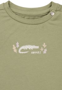 Zielona bawełniana koszulka z białą grafiką krokodyla oraz kolorowymi roślinami. Ma okrągły dekolt i zapięcie na zatrzask.