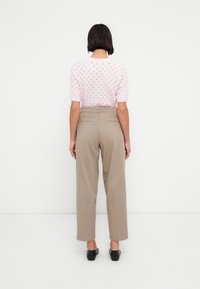 Ανοιχτό ροζ πλεκτό τοπ με κοντά μανίκια και σχέδιο διαμαντιού, σε συνδυασμό με ψηλόμεσο μπεζ παντελόνι. Μαύρα παπούτσια ολοκληρώνουν την εμφάνιση.