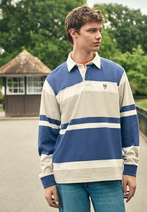 Langærmet rugbytrøje i marineblå og creme med horisontale striber og krave. Stoffet ser blødt ud med en afslappet pasform.