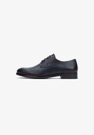 Zapato de vestir de cuero negro con un acabado liso, punta redonda, cinco ojales y un tacón bajo. Diseño simple con acentos mínimos.