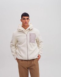 Hvid fleecejakke med lynlåslukning, der har en lys grå brystlomme og en cremefarvet hætte. Sammen med brune bukser.