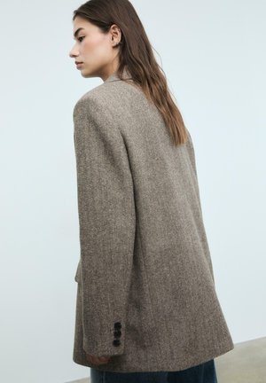 Hnědý houndstooth blazer s širokými rameny, strukturovaným střihem a třemi černými knoflíky na manžetě. Zadní pohled ukazující texturovanou látku.