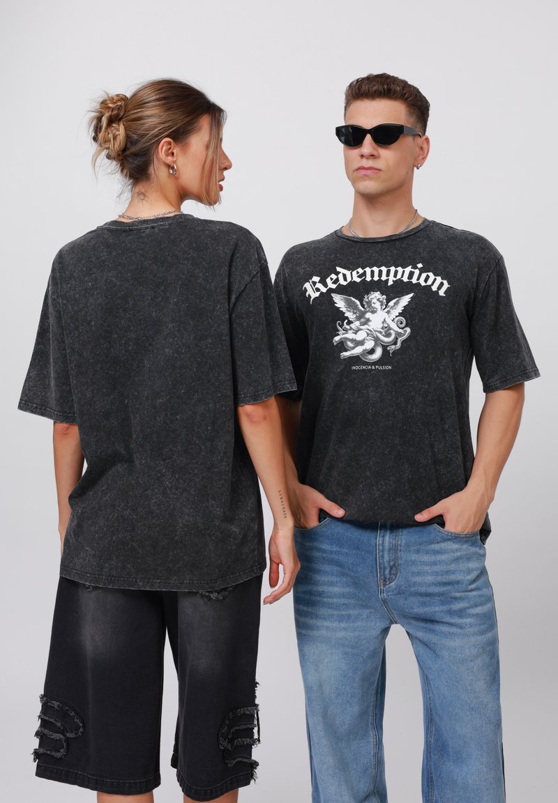 Svart, oversized t-skjorte med grafisk design foran, sammen med slitte denimshorts. Modellen bruker solbriller, som viser en uformell urban stil.