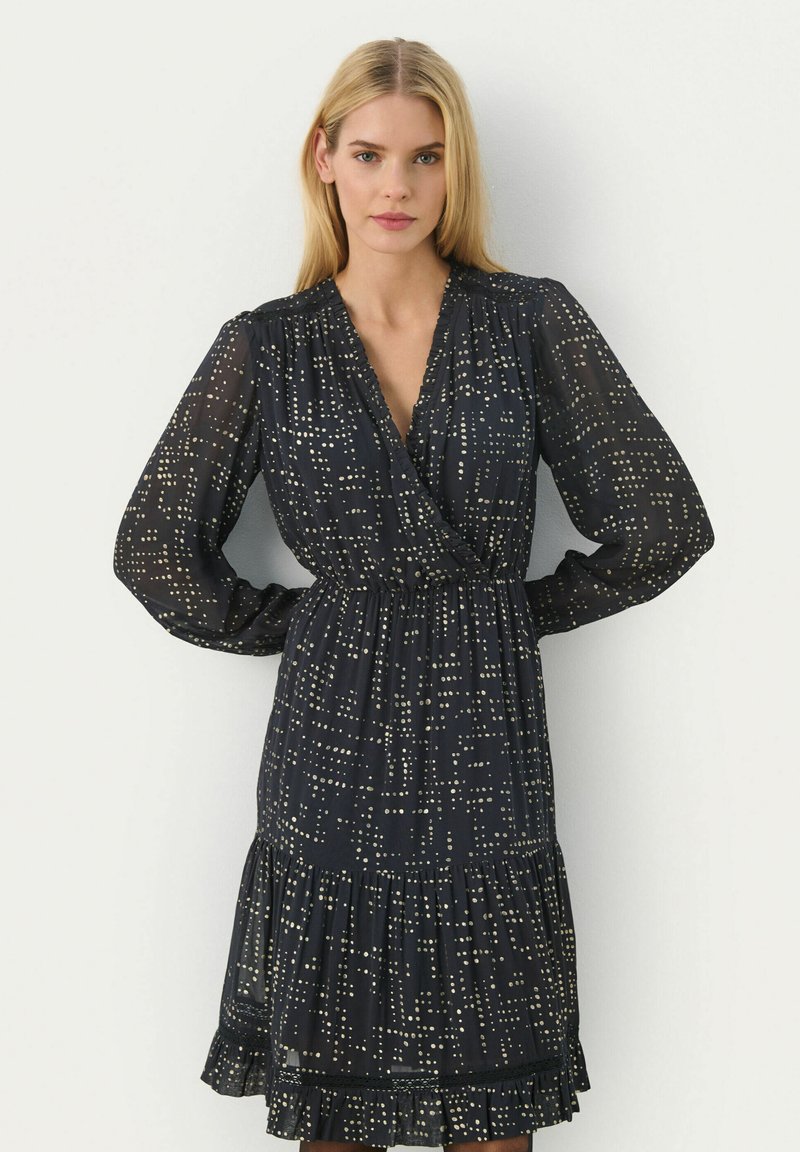 Rochie neagră cu model de puncte aurii, design înfășurat, mâneci lungi cu volane, talie elastică, tiv franjurat, fabricată dintr-un material ușor și transparent.