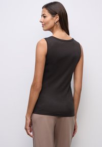 Sort ærmeløs top lavet af blødt stof, med en rund halsudskæring og en tætsiddende silhuet, parret med lyse bukser.