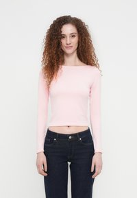 Ροζ ανοιχτόχρωμο cropped τοπ με μακριά μανίκια, κατασκευασμένο από απαλό ύφασμα, με λαιμόκοψη τύπου βάρκα και εφαρμοστή γραμμή, συνδυασμένο με σκούρο μπλε τζιν παντελόνι κανονικής γραμμής.