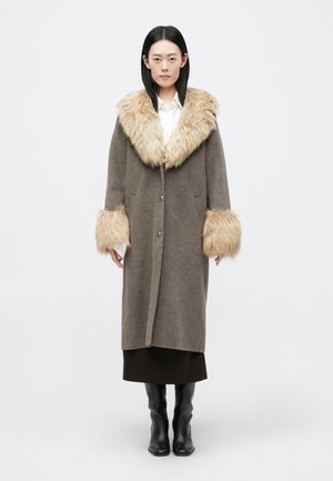 Casaco de lã castanho com um grande colarinho e punhos de pele sintética. Apresenta um corte reto, dois bolsos frontais e botões metálicos.