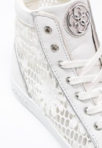 Zapatillas altas blancas con parte superior de malla con un patrón floral, acentos metálicos y una lengüeta de cuero texturizado. Ojetes plateados y cordones.