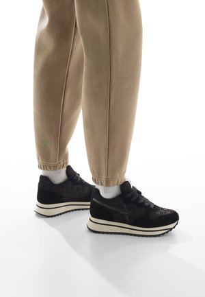 Scarpe da ginnastica nere in tessuto con una texture e accenti in suede. Suole bianche a contrasto e supporto per la caviglia imbottito. Indossate con pantaloni beige a gamba affusolata.