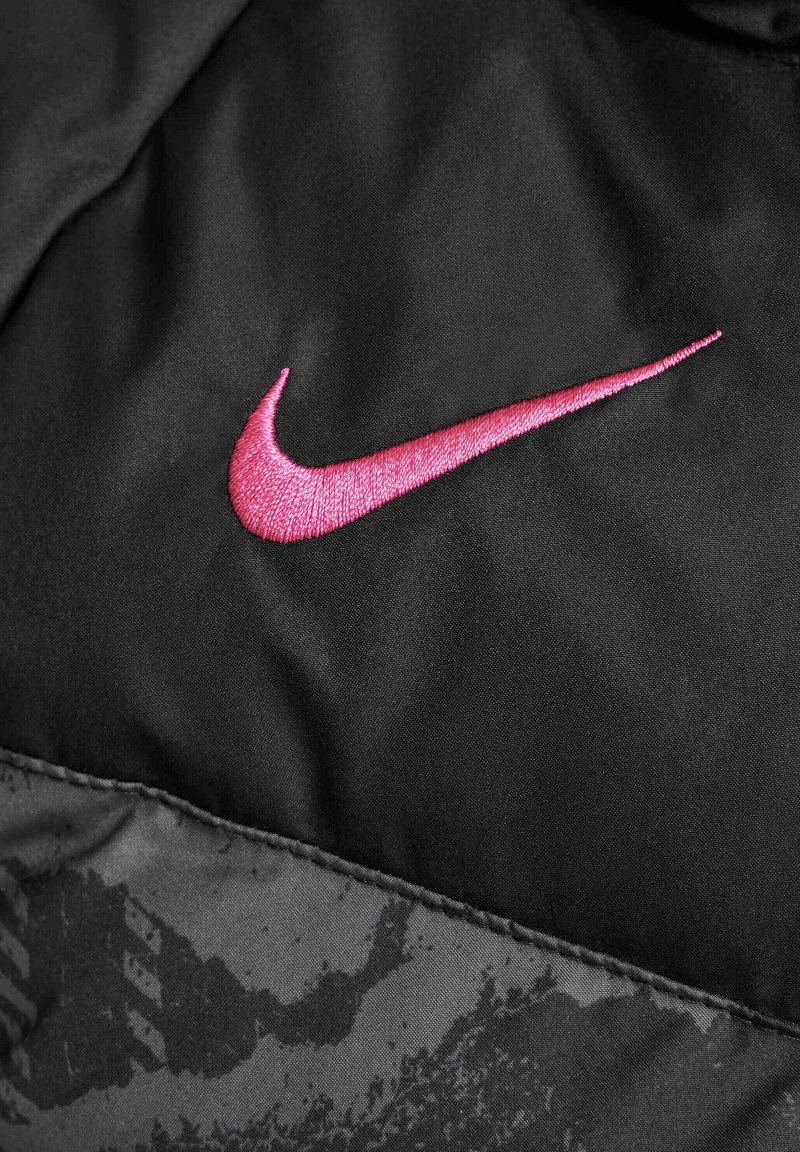Tejido negro con una textura suave presenta un destacado logo bordado de Nike en color rosa. La parte inferior muestra un sutil patrón negro.