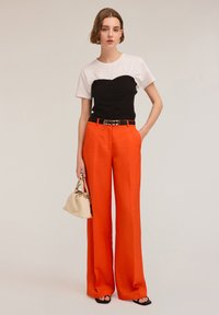 Top en blanco y negro con bloques de color y fruncido en el busto, combinado con pantalones anaranjados de pierna ancha de talle alto y un bolso color crema.