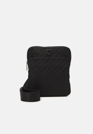 Sac messenger matelassé noir avec un logo triangulaire, poche avant zippée et bandoulière réglable. Texture lisse et design minimaliste.