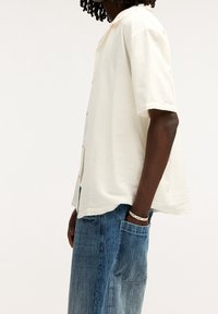 Kortere mouwen, lichtbeige overhemd in een ontspannen pasvorm, gemaakt van getextureerde stof met een knoopsluiting aan de voorkant, gecombineerd met blauwe denim cargobroek.