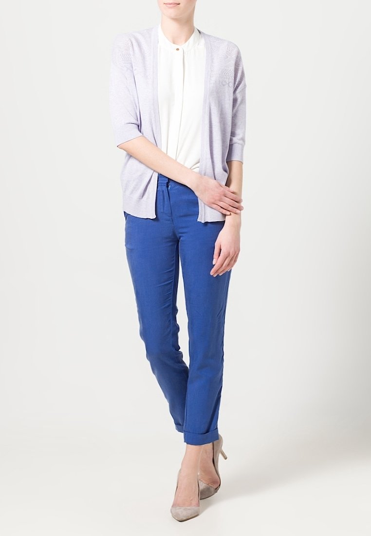 Ljust lila cardigan med trekvartslånga ärmar, lager på lager över en vit blus, kombinerat med blå byxor och beige klackar.