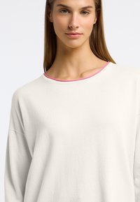 Witte lange mouwen top met een losse pasvorm, voorzien van een ronde halslijn afgewerkt met roze en een zachte textuur. Geen zichtbare patronen of hardware.