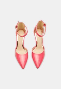 Tacones altos de charol rosa con puntera afilada, correas en el tobillo y un acabado brillante. Incluyen una plantilla acolchada para mayor comodidad.