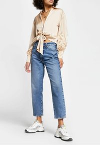 Beige satin blus med knyt framtill och långa ärmar, matchad med blå högmidjade raka jeans och vita sneakers med grå detaljer.