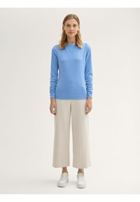 Maglietta azzurro chiaro maniche lunghe con scollatura rotonda, abbinata a pantaloni beige a gamba larga e sneakers bianche. Texture lisce in tutto.